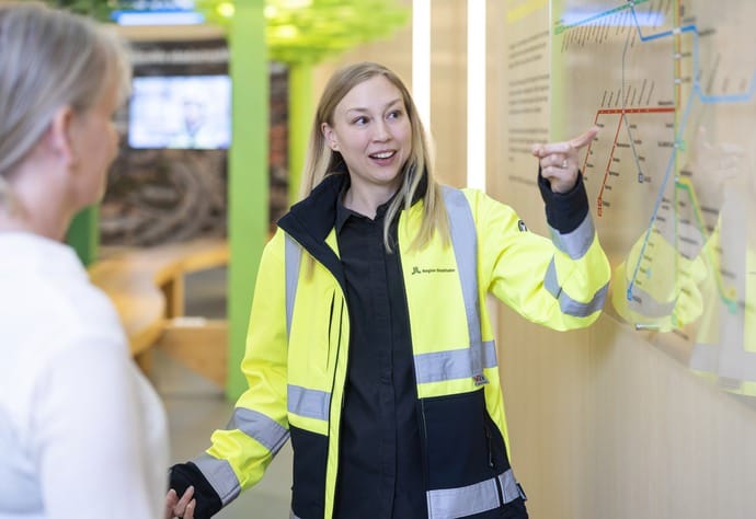 Kvinna med byggjacka pekar på en tunnelbanekarta.